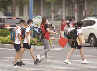 湛江一中金沙灣學校路口,家長志願者在引導學生安全過馬路.